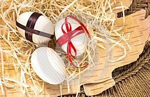 Easter eggs with ribbon and red flowers. Background birch bark and straw