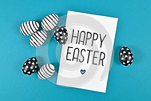 Easter eggs with simple black and white stripe and dot paintings with white card with `Happy Easter` text on blue background