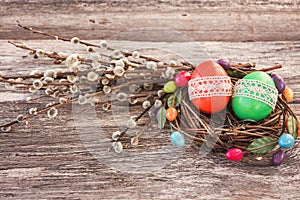 Easter eggs in small nest and willow branch on wooden background