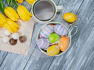 Easter eggs and tulips are on the table. View from above. Tea in a white cup and chocolates