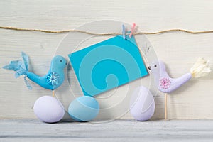 Easter eggs and two birds in pastel colors with a blank blue card on a white wooden background