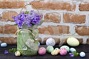 Easter eggs and violet bouquet in front of brick wall