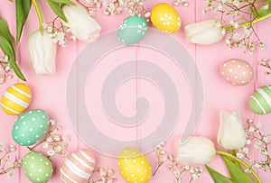 Easter eggs and white spring tulip flower frame against a pink wood background
