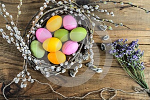 Easter eggs in willow nest, flowers over wooden rustic background