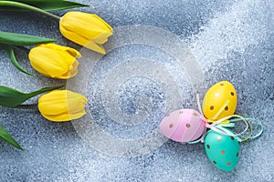 Easter eggs and yellow tulips on shabby blue and gray concrete background. Paschal decorations, holiday gift card