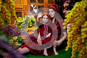 Easter. Family in rural wooden interior with flower in studio. Mother and daughter in maroon or red dresses of the