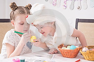 Easter festival: children paint easter eggs at the table. A boy in a rabbit costume looks cunningly at the work of the older siste photo