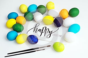 Easter festive colorful eggs on a white background with a greeting card calligraphy `happy easter`. eggs yellow, blue