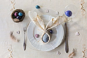 Easter festive spring table setting decoration, bunny ears shaped napkins, dyed eggs in nest, selective focus