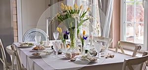 Easter festive spring table setting decoration, eggs in nest, fresh yellow tulips, marshmallows, selective focus banner