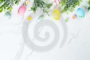 Easter composition with colored eggs and green plants on white background.