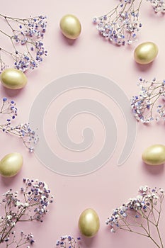 Easter frame of golden egg purple flowers on pastel pink. Top view with copy space