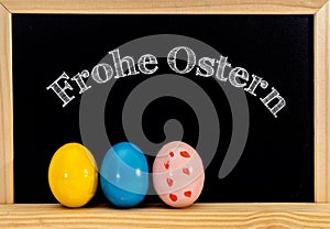 Easter frame with painted eggs and chalkboard. Happy Easter in white chalk. Happy Easter in German :