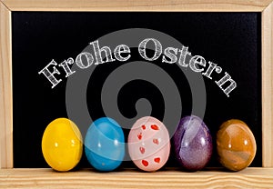 Easter frame with painted eggs and chalkboard. Happy Easter in white chalk. Happy Easter in German :