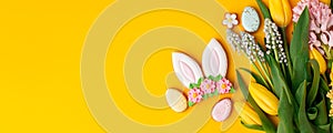 Easter gingerbread with icing, seasonal flowers on yellow table, festive Easter background web banner, copy space. Seasonal