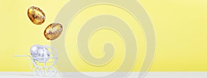 Easter golden and silver eggs levitation in the white baby stroller on a yellow background. Newborn concept. banner