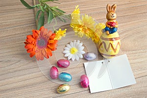 Easter greeting card with colored eggs candies, ceramic rabbit and flowers, on wood table with Copy space background