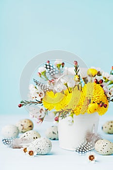 Easter greeting card with colorful flowers, feather and quail eggs on blue background. Beautiful spring composition.