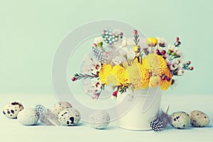 Easter greeting card with colorful flowers, feather and quail eggs on vintage blue background. Beautiful spring composition.