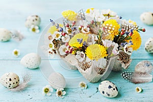 Easter greeting card with colorful flowers, feather and quail eggs on vintage turquoise table. Beautiful spring composition.