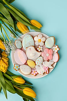 Easter greeting card with fresh tulip flowers, Gingerbread cookies - Easter eggs, bird, bunny and flowers on white plate, top view