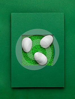 Easter greeting card   of green color balls, white egg, pink flower on green background. Styrofoam or Polystyrene foam background