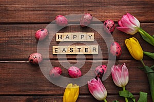 Easter greeting card. Tulips, pink colored quail eggs and inscription Happy Easter made from wooden letters on dark wooden
