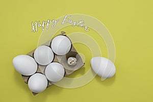 Happy Easter greeting white eggs in an egg carton and a toy baby chicken