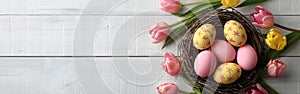 Easter Greetings: Pink Eggs and Yellow Tulips in Bird Nest Basket on White Wooden Table Background - Top View Flat Lay Banner