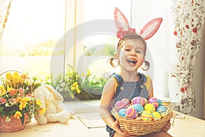 Easter. happy child girl with bunny ears and colorful eggs sitting at window in flowers