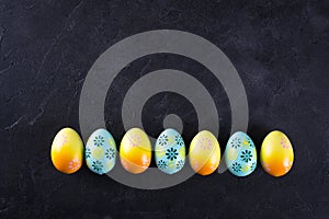 Easter holiday background with eggs. Top view of colorful painted chicken eggs plased in a row on black