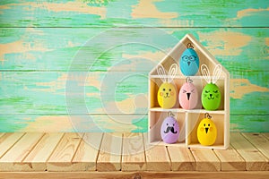 Easter holiday concept with colorful Easter eggs as cute bunny and chicken characters in toy house on wooden table