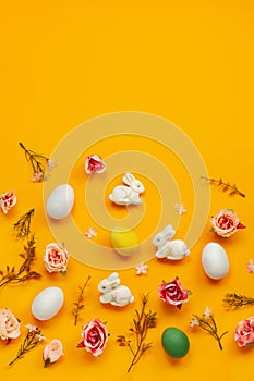 Easter holiday concept with cute handmade colorful eggs,  bunny and flowers on yellow background. Flat lay concept, top view