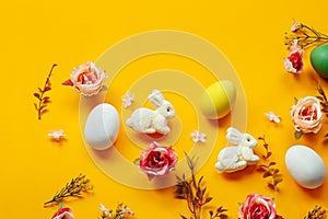 Easter holiday concept with cute handmade colorful eggs, egg tray, bunny and flowers on yellow background. Flat lay concept, top