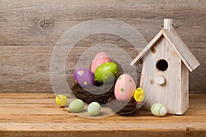 Easter holiday concept with eggs decoration, bird house and nest over wooden rustic background