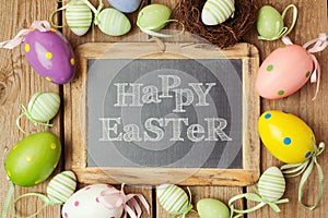 Easter holiday concept with eggs decorations and chalkboard on wooden background.