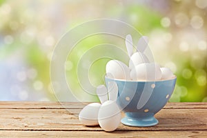 Easter holiday eggs with bunny ears on wooden table over garden bokeh background