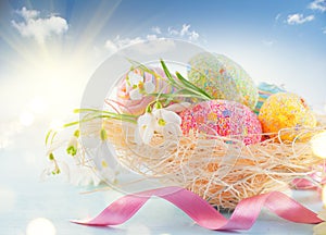 Easter holiday scene background. Traditional colorful eggs and spring flowers in the nest over blue sky