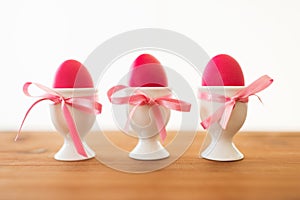 Three pink colored easter eggs in holders on table
