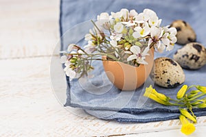 Easter interior decoration, bouquet of white yellow flowers in eggshell, quail eggs, blue napkin