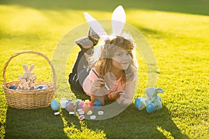 Easter kids boy in bunny ears paint easter eggs outdoor. Cute child in rabbit costume with bunny ears having fun in park