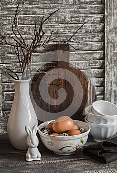 Easter kitchen still life - eggs in a bowl, a vase with dry twigs, ceramic rabbit, vintage crockery and cutting board