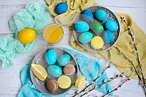 Easter layout. Yellow, blue and green eggs on plates, brown and yellow macaroons, lemons on a light background. View