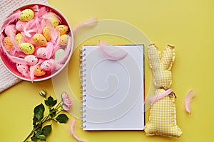 Easter mock up notepad. Pink bowl with colorful eggs, pink feathers, pink rose and handmade cute yellow bunny toy. Happy