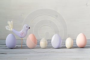 Easter pastel colored eggs and purple hand made bird on a light wooden background