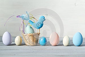 Easter pastel colored eggs and small basket with blue bird on a light wooden background