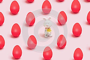 Easter pattern minimal funky concept. Little cute rabbit toy with many lovely red eggs. Pastel baby pink background