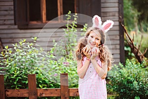 Easter portrait of happy child girl in funny bunny ears playing egg hunt outdoor