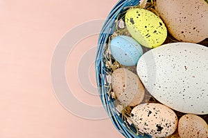 Easter quail eggs in a basket on a pale pink background.