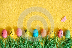 Easter quail white eggs on a yellow fluffy background and green grass made of paper. Easter card.Pink butterfly. Easter concept.